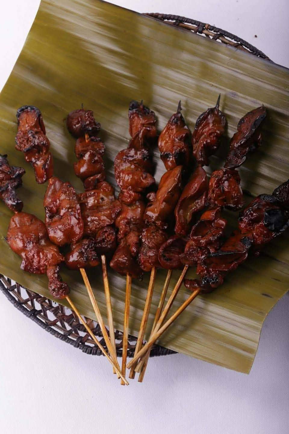 Filipino pork barbecue skewers fanned out on a banana leaf in a woven basket